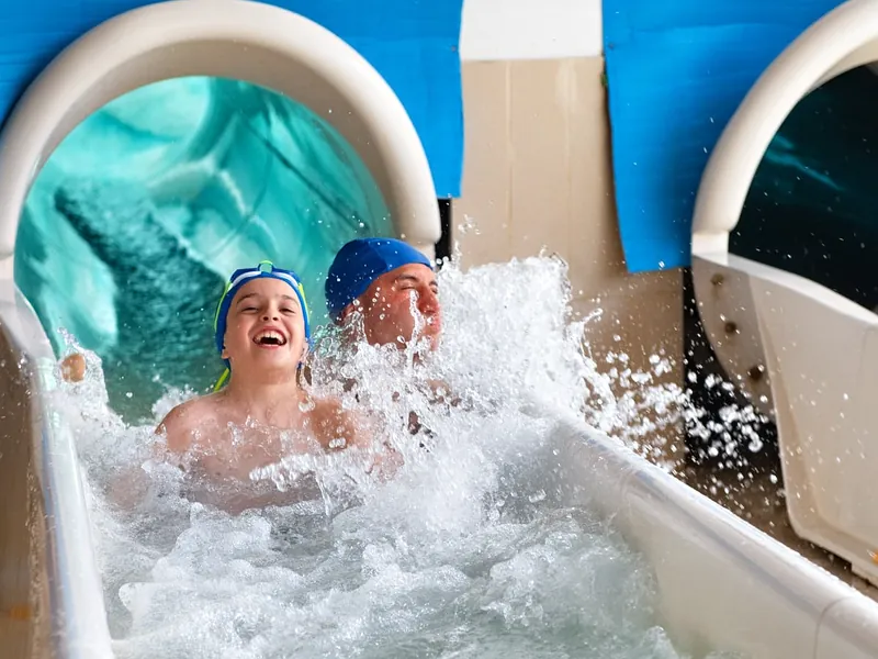 Un bambino ride all'arrivo dello scivolo, con un adulto subito dietro, tra gli schizzi